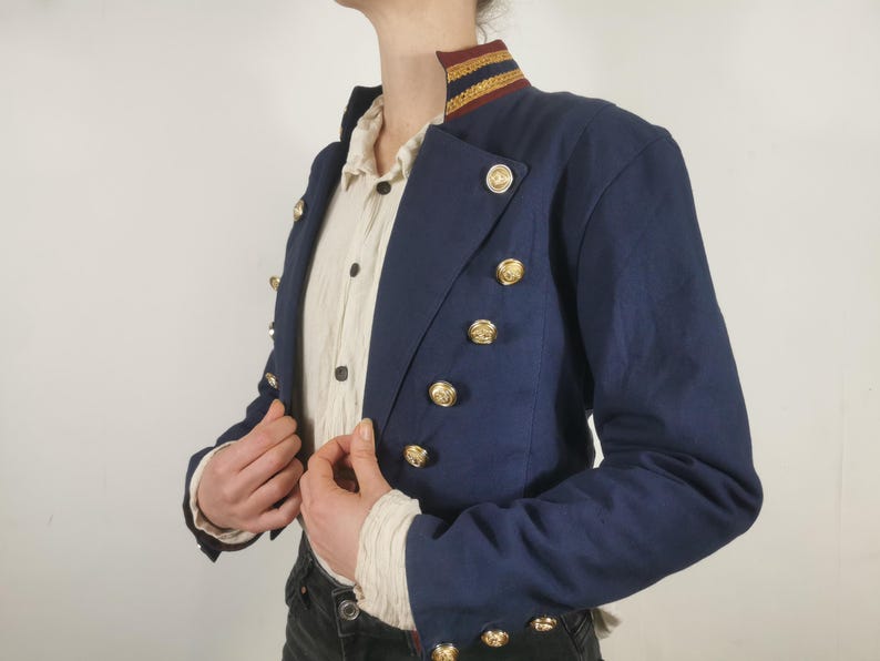 May include: A navy blue cropped jacket with gold buttons and a gold and red trim around the collar.