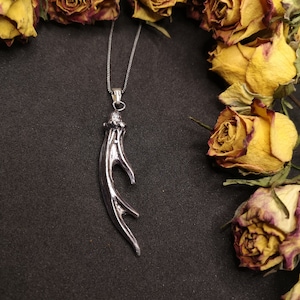 May include: A silver necklace with a detailed antler pendant. The necklace is displayed against a background of dried yellow roses.