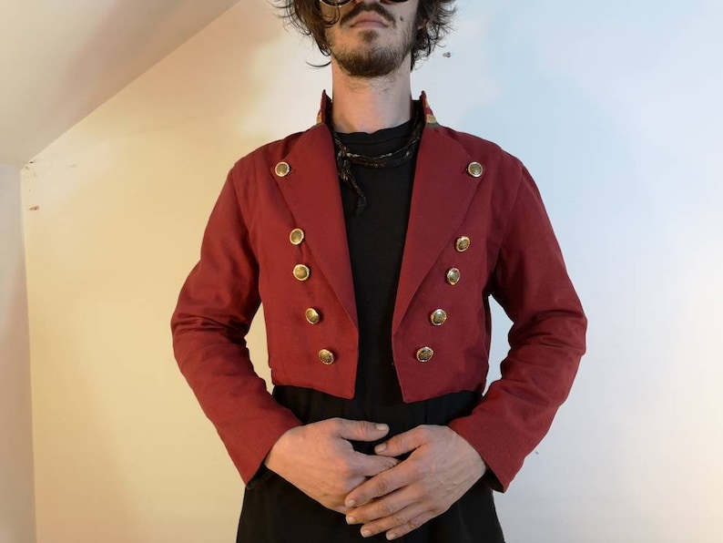 May include: A red cropped jacket with gold buttons and a black collar. The jacket has a fitted silhouette and a short length.