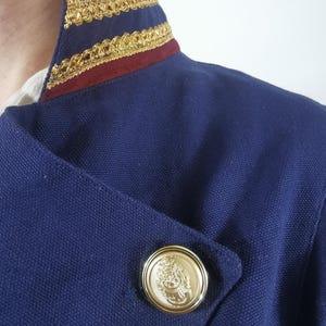 May include: A navy blue jacket with a burgundy and gold trim collar and a gold button with a design.