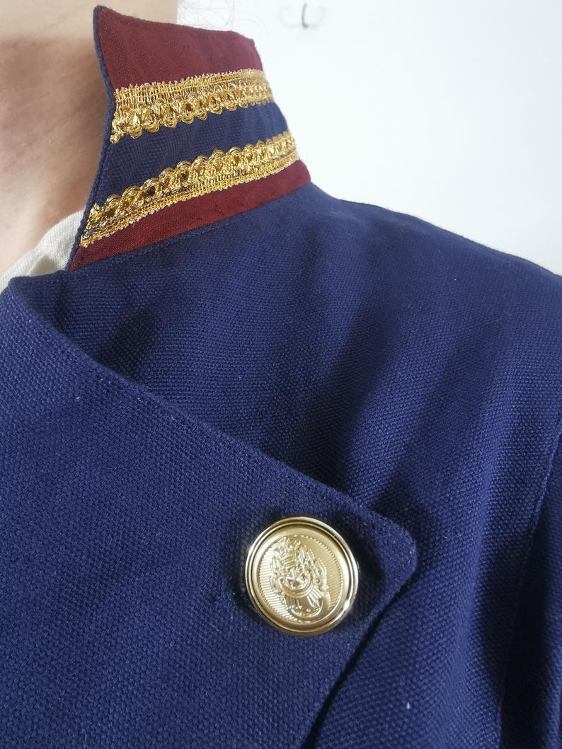 May include: A navy blue jacket with a burgundy and gold trim collar and a gold button with a design.