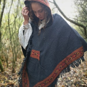 May include: A dark blue hooded poncho with a colorful geometric pattern around the edges and a pocket on the front. The poncho has a fringe trim.