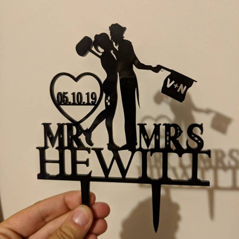 May include: Black silhouette of a couple kissing with a heart and the date 05.10.19. The text "MR. & MRS. HEWITT" is below the couple. The couple is holding a flag that says "V+N".