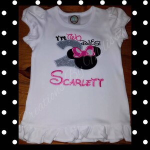 May include: White t-shirt with a silver glitter number 2, pink bow, and black Mickey Mouse ears. The text "I'm Two Disney!" is above the number and the name "Scarlett" is below.