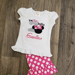 May include: White shirt with a silver glitter number two and the text "I'm two,  Disney" with a pink bow and black ears. The shirt has a white ruffle at the bottom. Pink and white polka dot pants with a white ruffle at the bottom.