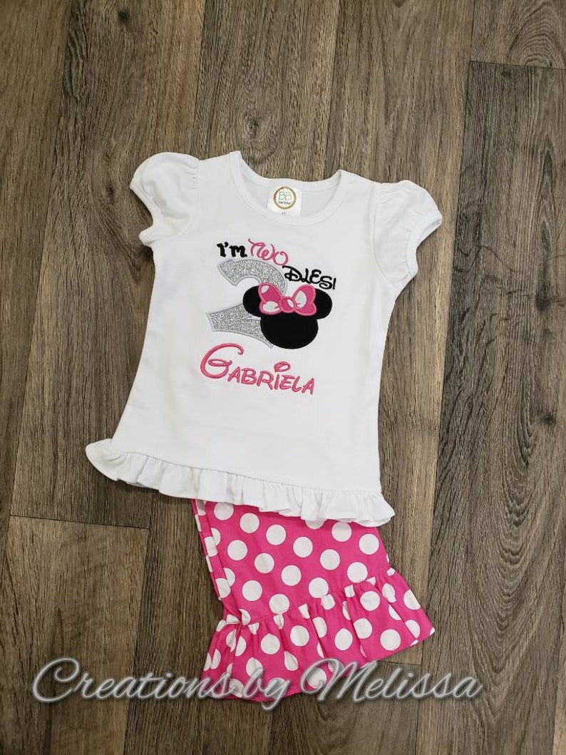 May include: White shirt with a silver glitter number two and the text "I'm two,  Disney" with a pink bow and black ears. The shirt has a white ruffle at the bottom. Pink and white polka dot pants with a white ruffle at the bottom.
