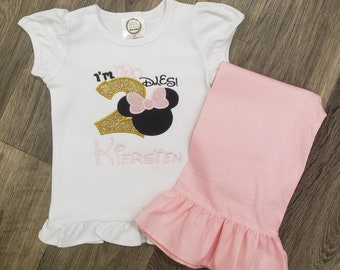 May include: A white short-sleeved shirt with a gold glitter number "2" and a pink bow on a black Minnie Mouse head. The shirt says "I'm Two Dies!" and "Kiersten" in pink embroidery. A pink polka dot skirt with a ruffle hem.