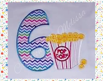 May include: A colorful chevron patterned number six with a red and white striped popcorn bucket with yellow popcorn on top. The text "POP CORN" is printed on the bucket.