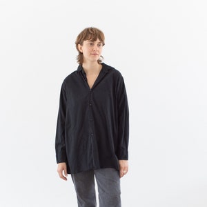 May include: A person wearing a black long-sleeved shirt with a collared neckline and gray jeans. They are wearing black loafers.