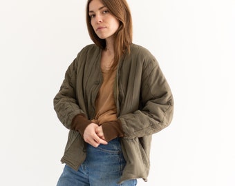 Puede incluir: Una mujer con una chaqueta acolchada marrón sobre una camiseta marrón y unos vaqueros azules.