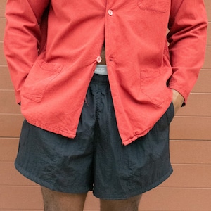 May include: A red button-down shirt with two front pockets and black shorts. The shirt has a collar and is unbuttoned at the top. The shorts are above the knee and have a drawstring.