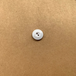 May include: A white button with two holes in the center. The button is on a brown background.