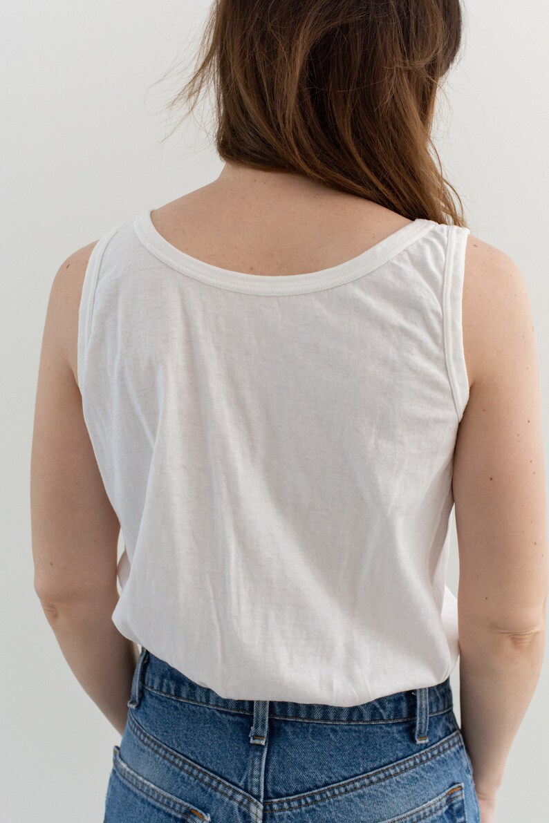 May include: A white sleeveless tank top with a scoop neck. The tank top is worn with blue denim jeans.