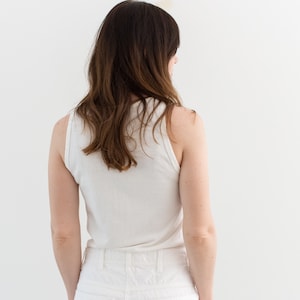 May include: A white tank top and white denim shorts. The person is facing away from the camera.