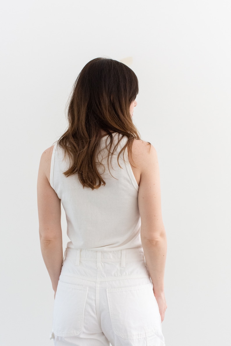 May include: A white tank top and white denim shorts. The person is facing away from the camera.