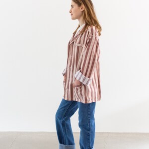 May include: A person wearing a striped, long-sleeved shirt with a white undershirt and blue jeans. The shirt has a brown and white striped pattern. The jeans are cuffed at the ankles, and the person is wearing brown suede boots.