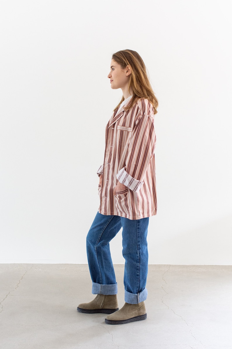 May include: A person wearing a striped, long-sleeved shirt with a white undershirt and blue jeans. The shirt has a brown and white striped pattern. The jeans are cuffed at the ankles, and the person is wearing brown suede boots.