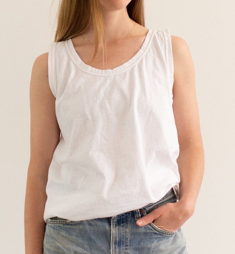 May include: A white sleeveless tank top with a scoop neck and a relaxed fit. The tank top is made of a soft, lightweight fabric and has a slightly distressed look.