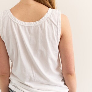 May include: A white sleeveless tank top with a scoop neck. The tank top is made of a soft, lightweight fabric and has a relaxed fit.