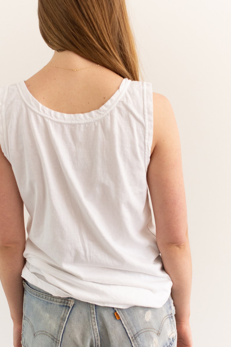 May include: A white sleeveless tank top with a scoop neck. The tank top is made of a soft, lightweight fabric and has a relaxed fit.