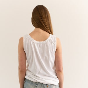 May include: A person wearing a white tank top and light blue jeans. The person is facing away from the camera.