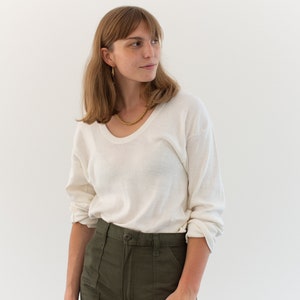May include: A long-sleeved, off-white scoop neck shirt paired with olive green utility pants featuring a button closure and front patch pockets. The shirt has a relaxed fit with sleeves that are rolled up at the forearms, and the pants have a high-waisted design.