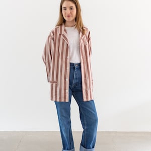 May include: A long-sleeved, button-down shirt with vertical stripes in shades of brown, tan, and white. The shirt is paired with a white t-shirt, blue jeans, and gray ankle boots. The jeans have rolled-up cuffs.