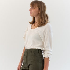 May include: A long-sleeve off-white scoop neck shirt with a lightweight texture paired with high-waisted olive green utility pants featuring a button closure, front patch pockets, and a structured waistband with belt loops.