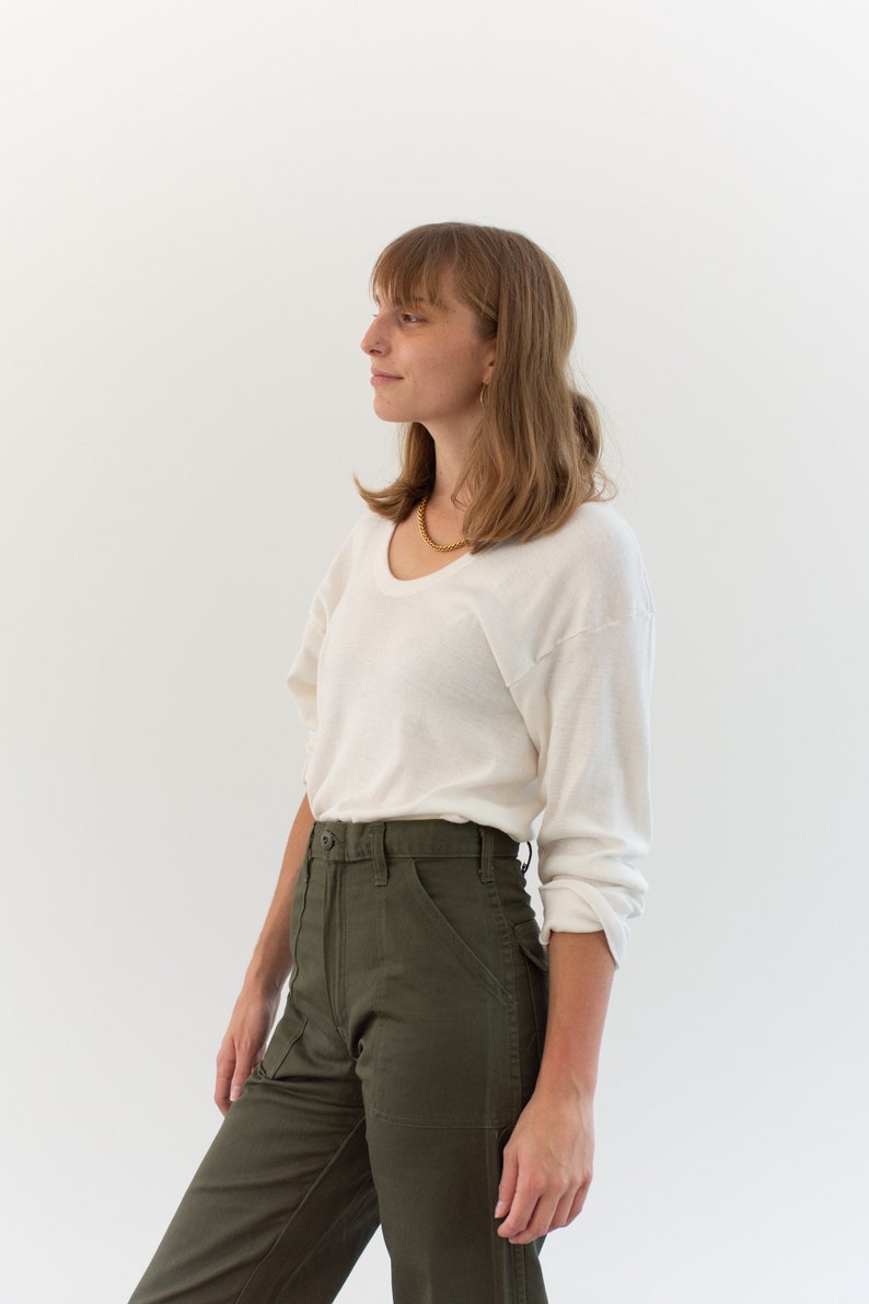 May include: A long-sleeve off-white scoop neck shirt with a lightweight texture paired with high-waisted olive green utility pants featuring a button closure, front patch pockets, and a structured waistband with belt loops.