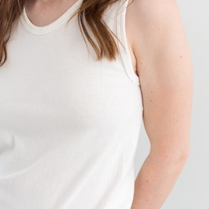 May include: A white sleeveless tank top with a round neckline. The tank top is made of a soft, stretchy fabric.
