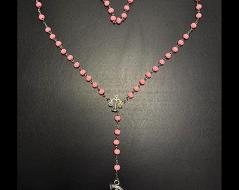 May include: Pink beaded rosary with a silver charm of a figure holding a scythe and a scale charm.