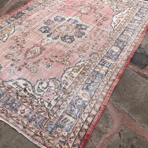 May include: A vintage pink and blue rug with a floral pattern and intricate border. The rug has a faded, distressed look, giving it a unique and charming character.