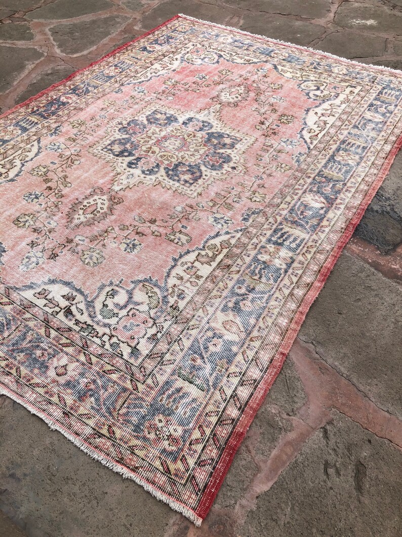 May include: A vintage pink and blue rug with a floral pattern and intricate border. The rug has a faded, distressed look, giving it a unique and charming character.