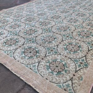 May include: A vintage rug with a floral pattern in shades of beige, green, and white. The rug has a fringed edge and is made of a woven material.
