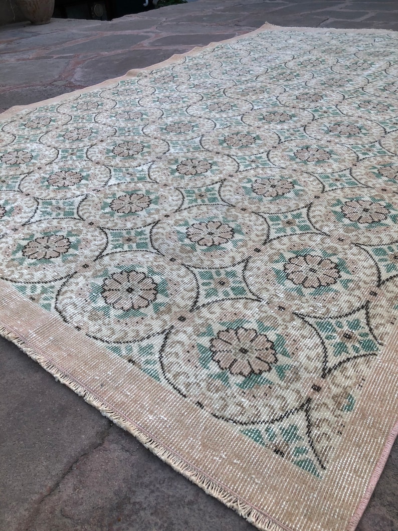 May include: A vintage rug with a floral pattern in shades of beige, green, and white. The rug has a fringed edge and is made of a woven material.
