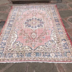 May include: A vintage pink and cream rug with a floral pattern and a blue border. The rug has a fringe around the edges.