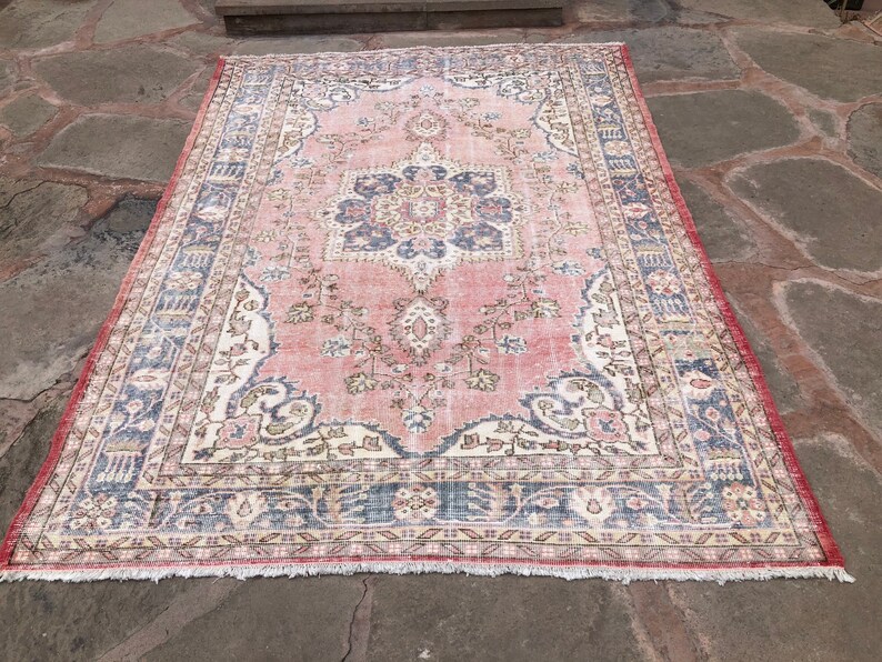 May include: A vintage pink and cream rug with a floral pattern and a blue border. The rug has a fringe around the edges.