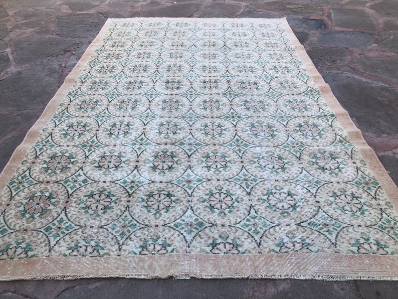 May include: A vintage rug with a cream background and a repeating pattern of green and brown floral motifs.