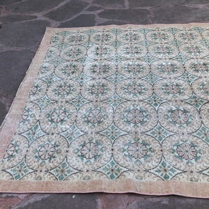 May include: A vintage rug with a cream background and a repeating pattern of green and pink floral motifs. The rug has a fringed edge.