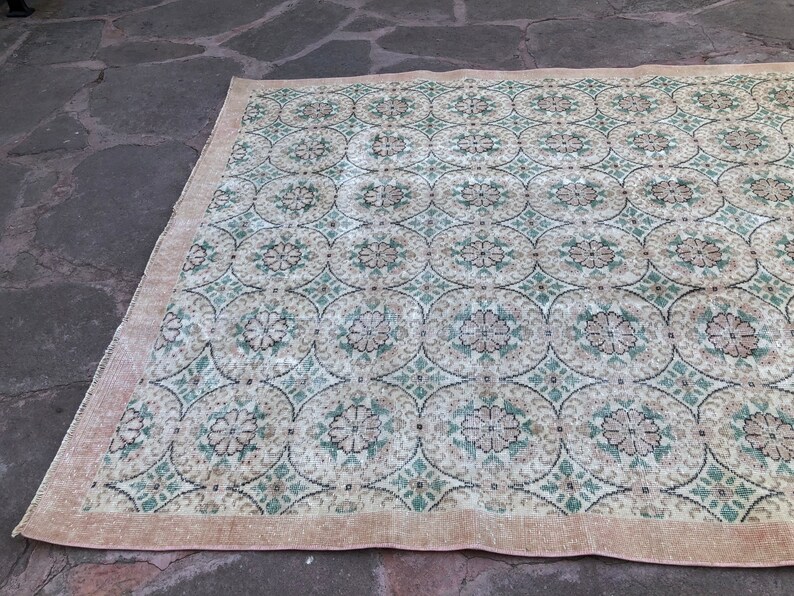 May include: A vintage rug with a cream background and a repeating pattern of green and pink floral motifs. The rug has a fringed edge.
