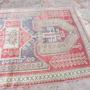 May include: A vintage Turkish rug with a geometric pattern in shades of red, beige, and gray. The rug has a fringe border and is woven with intricate details.