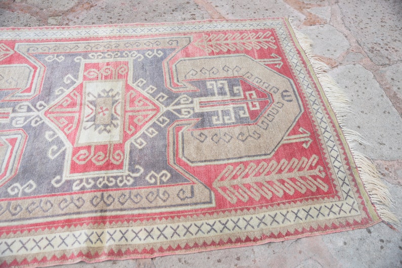 May include: A vintage Turkish rug with a geometric pattern in shades of red, beige, and gray. The rug has a fringe border and is woven with intricate details.