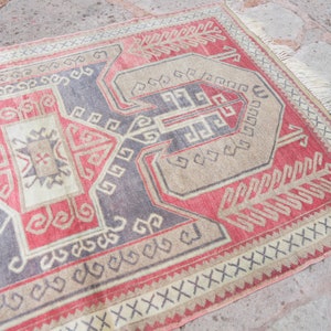 May include: A vintage Turkish rug with a geometric pattern in shades of red, beige, and gray. The rug has a fringe border and is woven with intricate details.