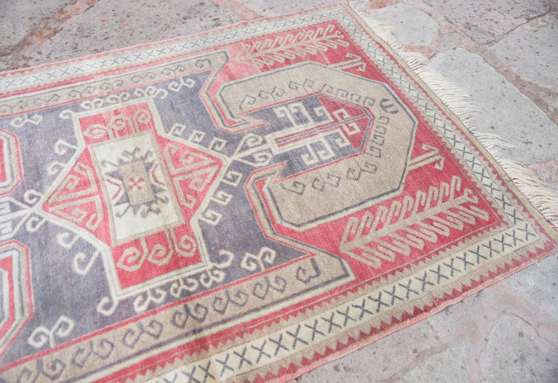 May include: A vintage Turkish rug with a geometric pattern in shades of red, beige, and gray. The rug has a fringe border and is woven with intricate details.