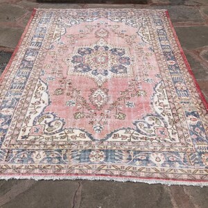 May include: A vintage rug with a pink background and a central medallion featuring floral designs. The rug has a faded appearance and a fringed border.