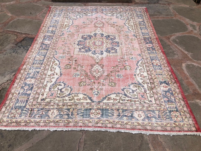 May include: A vintage rug with a pink background and a central medallion featuring floral designs. The rug has a faded appearance and a fringed border.