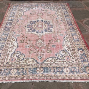 May include: A vintage pink and blue rug with a floral pattern and intricate border. The rug has a faded, distressed look, giving it a unique and antique feel.
