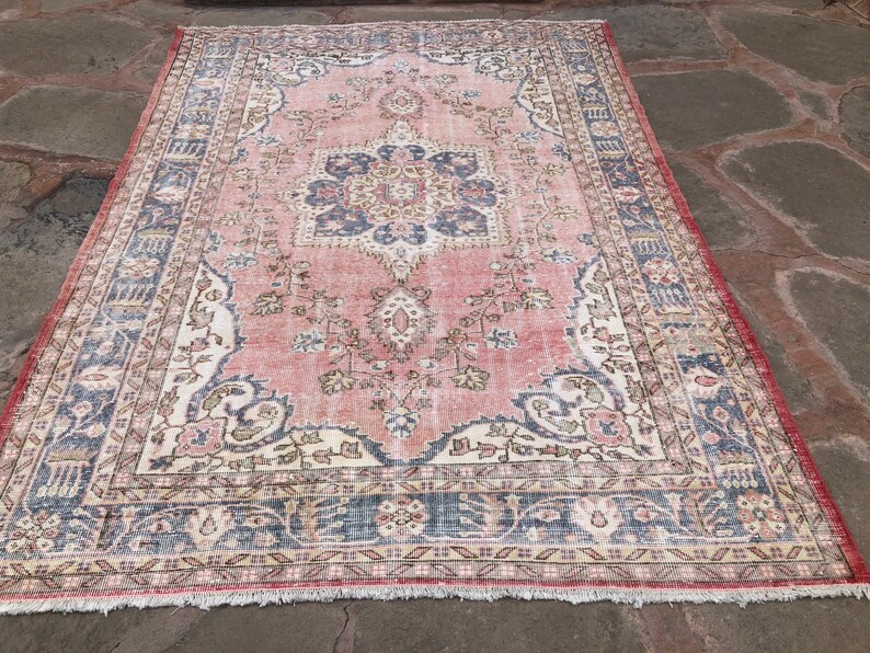 May include: A vintage pink and blue rug with a floral pattern and intricate border. The rug has a faded, distressed look, giving it a unique and antique feel.