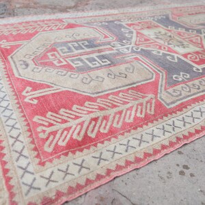 May include: A vintage Turkish rug with a red, beige, and gray geometric pattern. The rug has a fringe border and is made of wool.