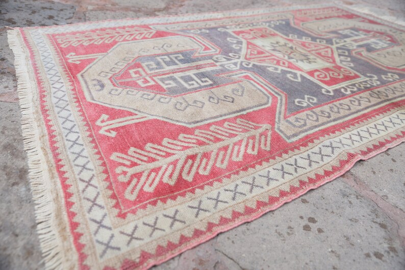 May include: A vintage Turkish rug with a red, beige, and gray geometric pattern. The rug has a fringe border and is made of wool.